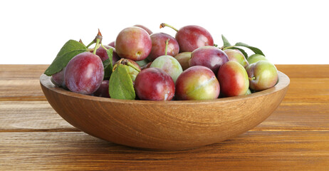 Fresh plums and green leaves in bowl on wooden table against white background