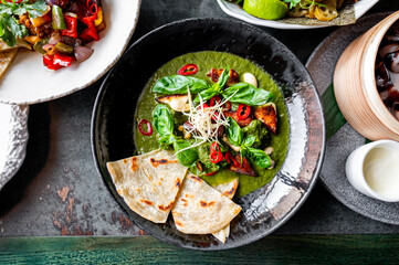 A vibrant bowl of green soup garnished with fresh herbs, tofu, and chili, served with flatbread on the side. Perfect for a healthy and delicious meal. Ideal for food photography and culinary blogs.