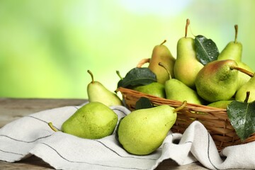 Fresh pears and leaves with water drops on wooden table against blurred green background, closeup. Space for text