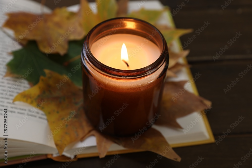 Wall mural burning candle, dry leaves and open book on wooden table, closeup. autumn atmosphere