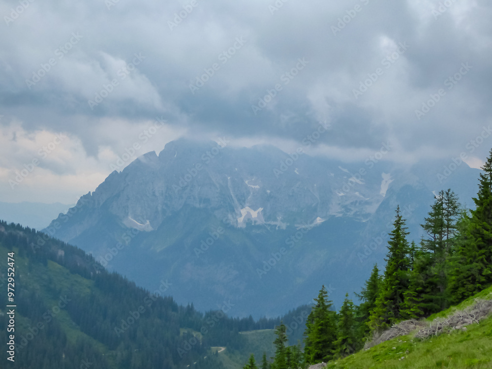 Wall mural hiking trail along alpine meadow with panoramic view of cloud covered mountain peaks in eisenerz alp