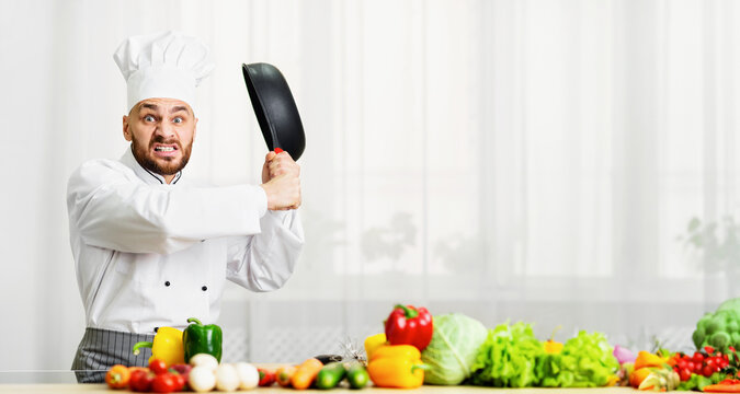 Mad Professional Chef Guy Raising Frying Pan Threateningly Grimacing Standing In Kitchen. Free Space For Text