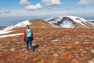 Fototapeta premium Hiker woman on scenic hiking trail over snow covered alpine meadows and rolling hills to snow-capped mountain peak Lenzmoarkogel, Gleinalpe, Lavantal Alps, Styria, Austria. Wanderlust in Austrian Alps