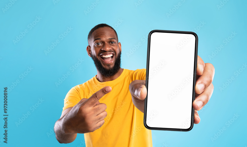 Poster Mobile advertisement. Overjoyed black man pointing at cellphone with empty white screen on blue studio background, mockup for app or website. Cellphone display template