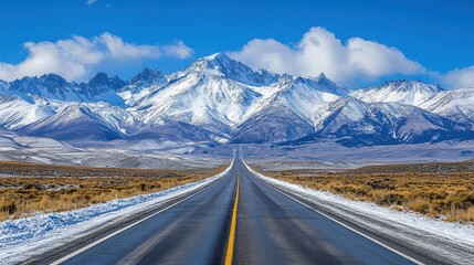 Naklejka premium Straight Road Leading to Snowy Mountains Under Clear Blue Skies