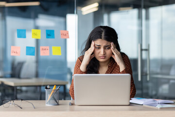 Upset and tired woman sitting at workplace inside office, business woman leaning on arms reading...