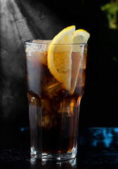 Cocktail in a highball with cola and lemon slices against a dark background