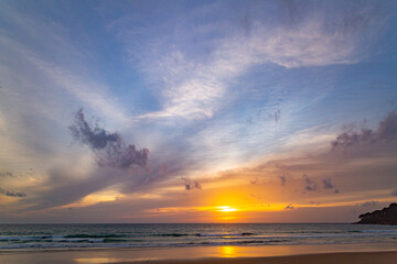 A stunning sunset over the ocean with soft golden light reflecting on the water, featuring silhouettes of people walking along the shore. Water flows from a small stream into the sea.