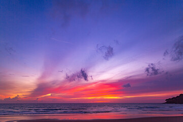 A serene beach scene at dusk, showcasing a vivid sunset with colorful clouds reflected on the calm waters and wet sand. amazing sky in sunset over Karon beach Phuket. sweet sky background.
