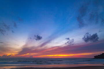 A serene beach scene at dusk, showcasing a vivid sunset with colorful clouds reflected on the calm waters and wet sand. amazing sky in sunset over Karon beach Phuket. sweet sky background.