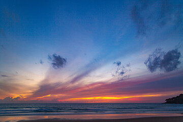 A serene beach scene at dusk, showcasing a vivid sunset with colorful clouds reflected on the calm waters and wet sand. amazing sky in sunset over Karon beach Phuket. sweet sky background.