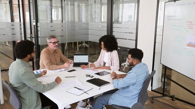 A team of four professionals are gathered around a white table in a modern office, indicative of a cooperative and strategic business meeting. Productive meetings and brainstorming concept