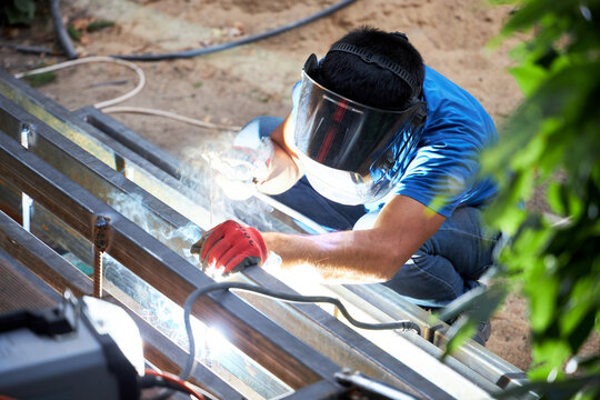 a worker welds a metal ladder in the garden