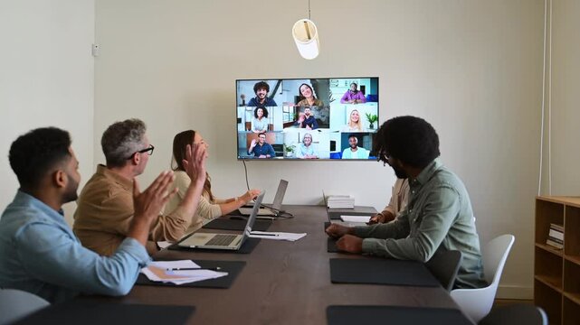 A team actively engages with remote colleagues via a large screen, illustrating the modern hybrid work model where technology bridges the gap between in-office and remote team members