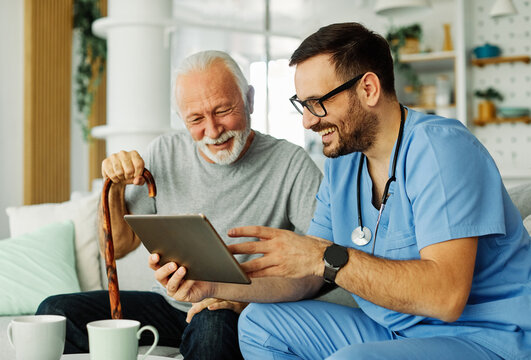 nurse doctor senior care tablet computer technology showing caregiver help assistence retirement home nursing elderly happy laughing man
