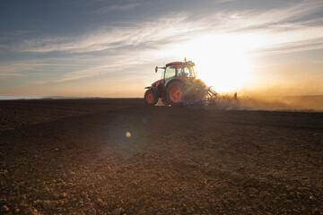 A red tractor prepares the land with a plow.
