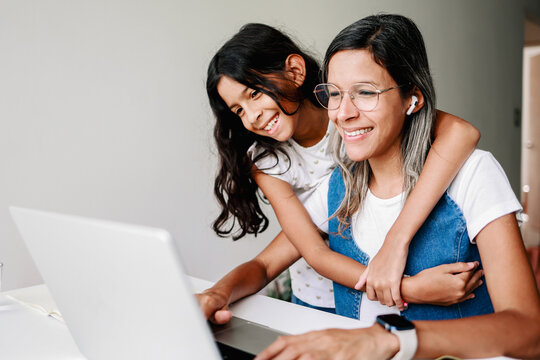 Black working mother using computer laptop at home office. Happy daughter hugging mom. Family love relationship
