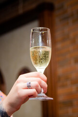 A glass of champagne or sparkling wine, held by a hand, champagne bubbles visible in the glass