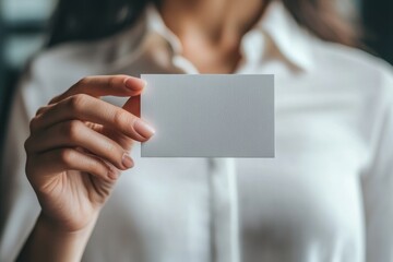Obraz premium Close-up photo of a woman's hand holding a blank business card, wearing a white-colored shirt, with a blurred background Generative AI