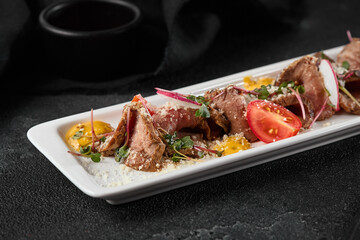 Gourmet Beef Roast with Fresh Vegetables on Elegant White Plate Against Dark Background