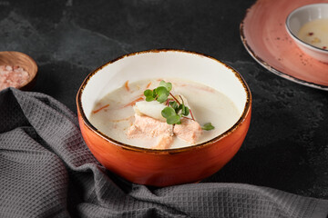 Creamy Fish Soup in Rustic Orange Bowl on Dark Background with Grey Napkin and Pink Himalayan Salt