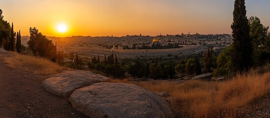 A panoramic view of Jerusalem at sunset, with the Dome of the Rock visible in the distance and a golden sky above.