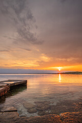 Beach in the morning. Sunrise, pebble beach on a rocky coast. The sky is reflected in the water of a bay. Natural spectacle of a Mediterranean landscape, island of Vir, Zadar, Dalmatia, Croatia, Adria