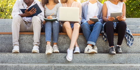 Fototapeta premium Cropped of international students doing homework on stairs in city, using laptop, taking notes, education concept
