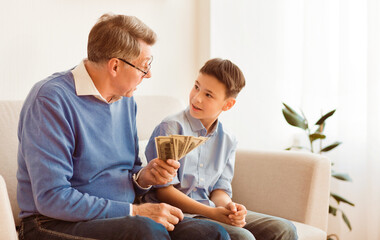 Financial Literacy. Elderly Man Explaining Grandson Value Of Money, Talking About Savings And Banking Sitting On Sofa Indoor
