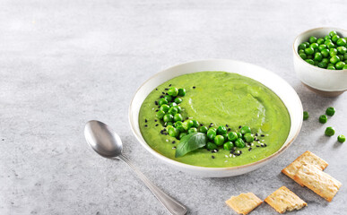 Green pea cream soup with crackers on a gray table. Top view. Copy space.