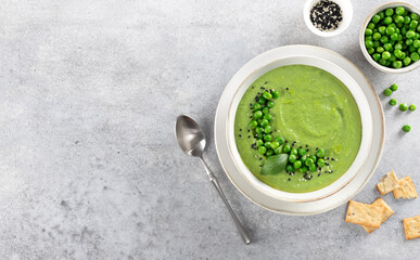 Green pea cream soup with crackers on a gray table. Top view. Copy space.