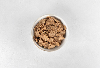 Whole grain corn flakes in a white bowl on a white background. Fitness breakfast. Top view. 