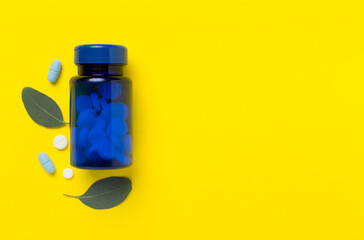 Bottle with pills and green leaves on color background, top view