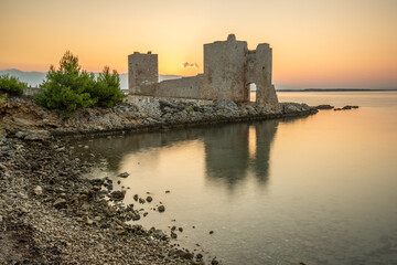 Castle ruins at dawn. Bay on the Mediterranean Sea with calm water at sunrise. Reflection of the...