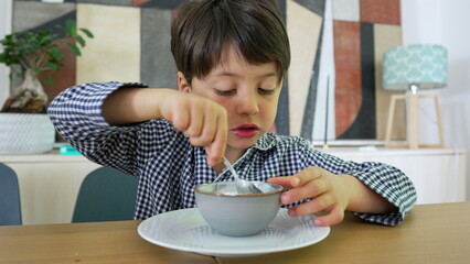 Young boy focused on eating a bowl of yogurt at the dining table, capturing a moment of concentration and contentment in a bright and inviting home setting