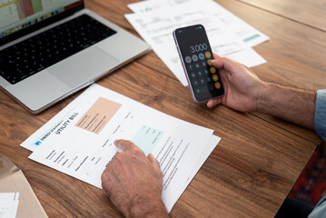 Close-up of a man calculating household utility bills using a smartphone. Financial management and...