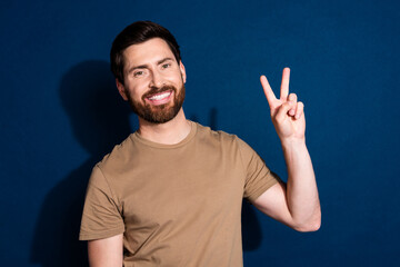 Naklejka premium Photo portrait of young guy brunet hair model in beige t shirt showing v sign symbol peace and friendly isolated on dark blue color background