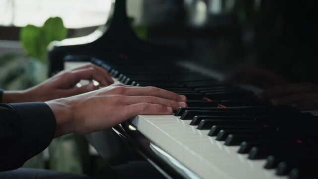 Cinematic closeup side view of young male hands expertly playing black grand piano in a beautiful indoor setting with background window light