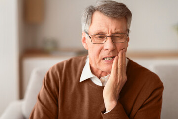 Elderly Man Having Toothache Touching Cheek Suffering From Pain Sitting On Sofa At Home. Selective...
