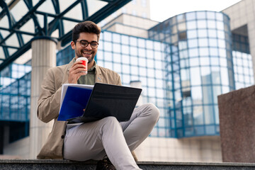 Smiling Businessman Working on Laptop Outside Office Building