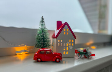 There is a candlestick house, a red retro car and a Christmas tree on the windowsill. Window sill...