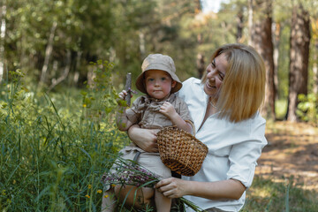A young beautiful woman and a little boy gather flowers together in a clearing in the forest