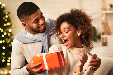 Xmas surprise. Afro man giving Christmas present to girlfriend, celebrating holidays together