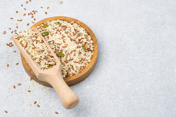 A mixture of flax, sesame, sunflower and pumpkin seeds in a wooden bowl and in a spatula on a light...
