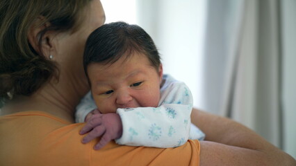 Grandmother gently holding her newborn grandchild close to her shoulder, offering security and comfort. baby’s calm demeanor highlights the nurturing care and bond between them