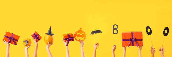 Women with Halloween gifts and pumpkins on yellow background