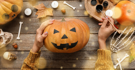 Woman with painted Halloween pumpkin at wooden table