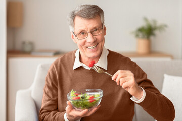 Healthy Nutrition. Senior Man Eating Fresh Vegetable Salad Smiling At Camera Sitting On Couch At Home. Selective Focus