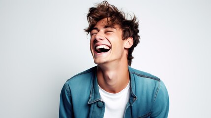 Fototapeta premium A young man in a denim jacket laughs exuberantly in front of a minimalist white background.