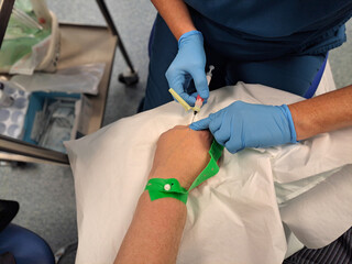 Blood test sample: Nurse wearing blue gloves uses syringe and needle to draw blood from vein on...